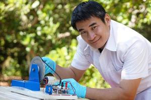 Asian man wears blue gloves demonstrate science experiment about electricity circuit from dynamo kit for teaching. Concept, science subject, project work. Experiment, education. Outdoor class. photo