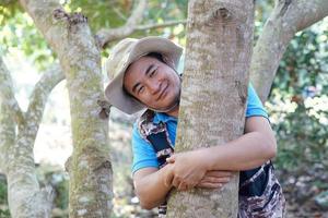 Handsome Asian man botanist hugs trunk of tree in forest. Concept, Love nature and protecting, Forest ,ecology and environment conservation. photo