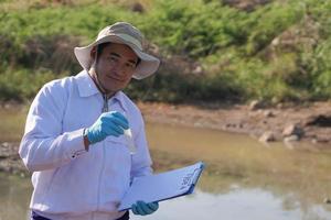 Asian man environment researcher holds tube of sample water to inspect from the lake. Concept, explore, analysis water quality from natural source. Ecology field research. photo