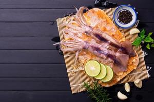 Raw squid on ice with lemon garlic spice salad on black wooden table background, fresh squid for cooked food at a kitchen restaurant or seafood market photo