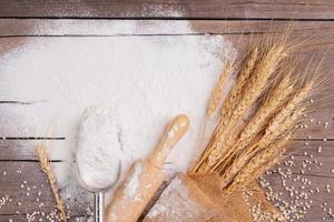 Flour and ears of wheat, barley, cooking, bread, and cookies were arranged on the wooden table background in a rustic kitchen. Top view. photo