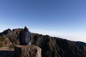 turista se sienta a montaña parte superior en contra el antecedentes de majestuoso montañas, Madeira, Portugal foto