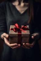 Gift box with red ribbon bow in female hands. photo