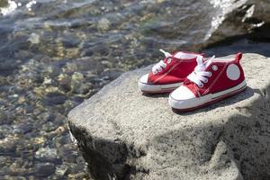 un par de para niños rojo zapatillas estar en un rock por el mar. foto