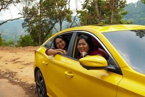 Middle-aged Asian woman and friend with a lover's yellow sedan. Everyone smiled happily. to travel the mountains on a summer vacation together.soft and selective focus. photo