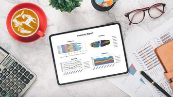 Tablet with charts and reports on office desk workplace. Top view flat lay. photo