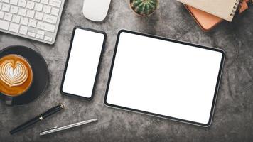 Dark office desk workplace with blank screen tablet and smartphone, keyboard, mouse, notebook, pen and cup of coffee, Top view flat lay with copy space. photo