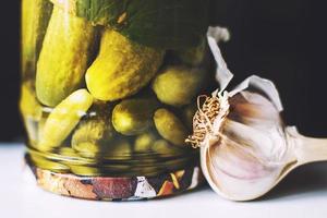 pickled cucumbers in a glass jar with garlic on a dark background. inverted jar with cucumbers close photo