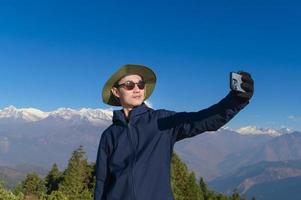 A young traveler takes a selfie or a video call while standing a top a mountain. photo