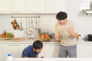 contento joven asiático padre y hijo haciendo desayuno juntos. juguetón en cocina a hogar foto