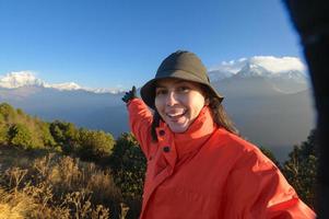 A young traveler takes a selfie or a video call while standing a top a mountain. photo