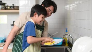 Happy smiling Young Asian father and son washing dishes in kitchen at home photo