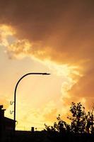 Sunset or dawn sky, yellow clouds with rays and hidden sun with black roof silhouette, lantern. Verical. Copy space photo