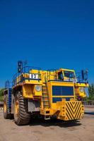 Heavy yellow quarry tractor at repair station at sunny cloudless day photo