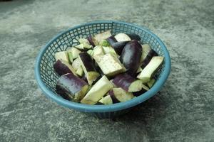 pieces of purple eggplant in a green plastic container on a gray background. top angle. photo