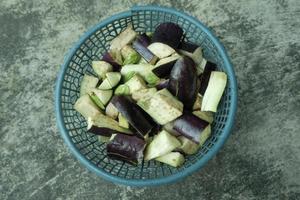 pieces of purple eggplant in a green plastic container on a gray background. top angle. photo