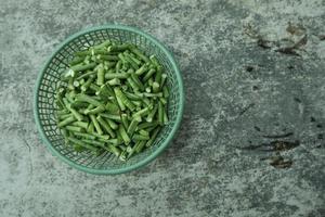 largo frijol piezas en un verde el plastico envase en un gris antecedentes. parte superior ángulo. foto