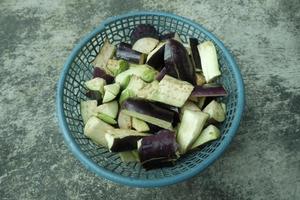 pieces of purple eggplant in a green plastic container on a gray background. top angle. photo