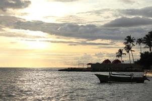 Silhouette of a fisherman's boat and a coconut tree on the beach with a sunset background photo