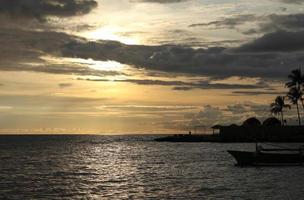 Silhouette of a fisherman's boat and a coconut tree on the beach with a sunset background photo