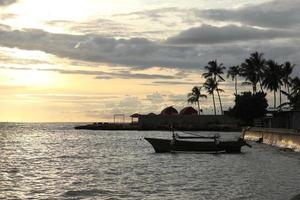 Silhouette of a fisherman's boat and a coconut tree on the beach with a sunset background photo