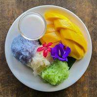 Fresh sweet mango served with 3 colors sticky rice and coconut milk on white dish. photo