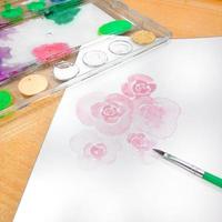 Watercolor paints and brushes on a white sheet of paper with a rose drawing. photo