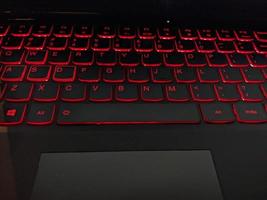 Keyboard with red backlight texting by hand. The photo is suitable to use for laptop background activity and service content media.