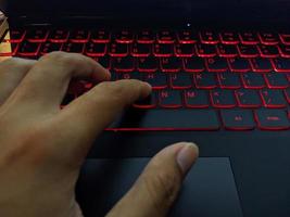 Keyboard with red backlight texting by hand. The photo is suitable to use for laptop background activity and service content media.