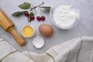 Ingredients baking flour eggs rolling pin berries kitchen textiles on gray background. Cookie pie or cake recipe mockup. Background preparation for culinary baking. photo