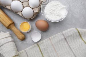 Baking cooking ingredients flour eggs rolling pin and kitchen textiles on gray concrete background. Cookie pie or cake recipe mockup photo