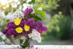 Spring or summer background. A bouquet of lilacs and yellow tulips in a glass jar on the table. Beautiful flowers on a green background. photo