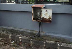 Jakarta, Indonesia - April 10th, 2023 - Outdoor electrical opened old box isolated on gray walls. Messy visible electricity power cable photography. Not maintained facility. photo