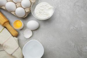 Baking cooking ingredients flour eggs rolling pin and kitchen textiles on gray concrete background. Cookie pie or cake recipe mockup photo