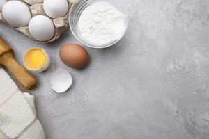 Baking cooking ingredients flour eggs rolling pin and kitchen textiles on gray concrete background. Cookie pie or cake recipe mockup photo