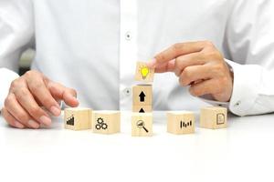 Hand holding a wooden block cube the top one with light bulb icon symbol and wooden blocks various icon symbols laying on white. Target of business and innovative idea concept. photo
