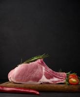 Raw pork tenderloin on the bone and spices on a wooden cutting board on a black background. Portion for lunch and dinner photo