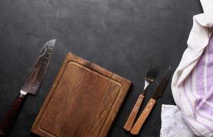 Empty wooden kitchen cutting board, knife and fork with wooden handle on black background, top view photo