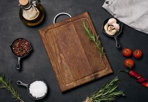 Empty brown wooden board and spices on black table, top view photo