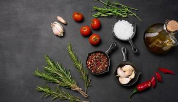 miniatura sartenes con especias, sal, negro pimienta y fragante pimienta, un puntilla de Romero en un negro mesa. especias para Cocinando foto