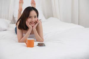 Portrait of white Asian woman with tattoo resting in bed to rest and relax inside white bedroom on her holiday, holiday morning concept. photo