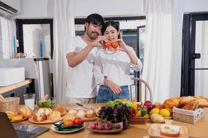 joven asiático Pareja Cocinando con frutas y vegetales y utilizando ordenador portátil en el cocina a cocinar comida juntos dentro el familia felizmente, familia concepto. foto