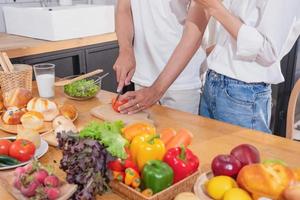 joven asiático Pareja Cocinando con frutas y vegetales y utilizando ordenador portátil en el cocina a cocinar comida juntos dentro el familia felizmente, familia concepto. foto