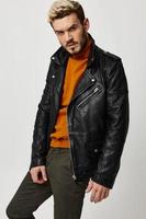 stylish guy in a leather jacket and trousers and in a sweater posing on a light background photo