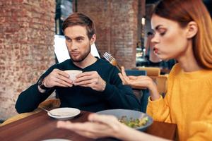 mujer teniendo cena a un mesa en un café y un hombre con un taza de café en el antecedentes foto