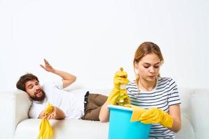 woman with a bucket in rubber gloves at home husband lies on the couch cleaning photo