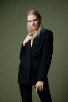 A blonde lady holds a jacket by the collar with one hand posing on a green background in the studio. A concept for clothing brands. Cool offer for fashionable suits photo