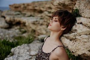 mujer en vestir corto Corte de pelo posando sentado en el rocas al aire libre inalterado foto