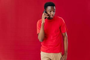 hombre de africano apariencia en un rojo camiseta con un teléfono en el manos foto