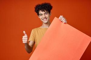 Cheerful man with curly hair poster in hands advertising studio photo